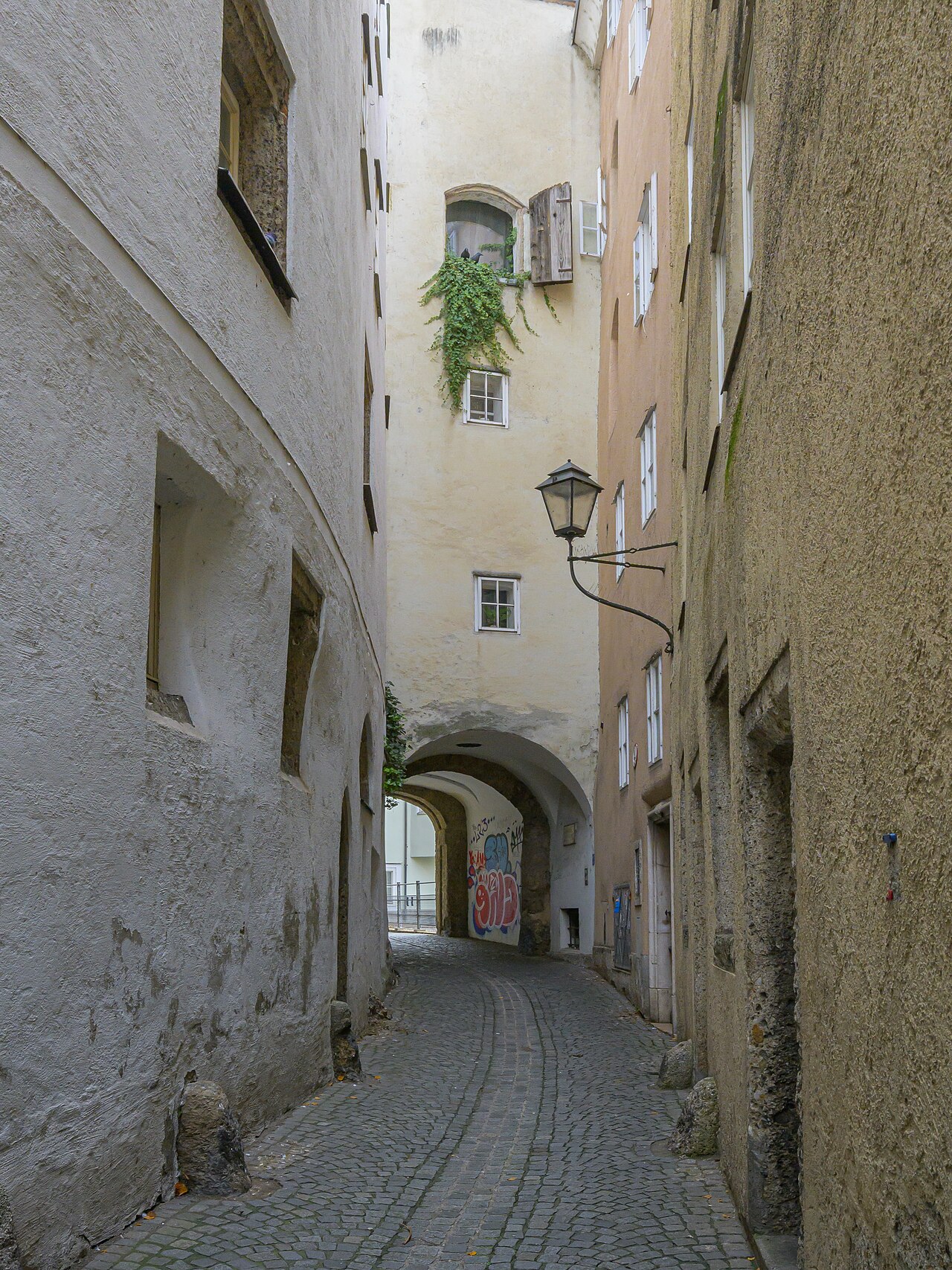 The narrow cobbled Steingasse between tall plain house walls, a wall lantern at right and, at the end of the lane, the arched passage of the Inneres S