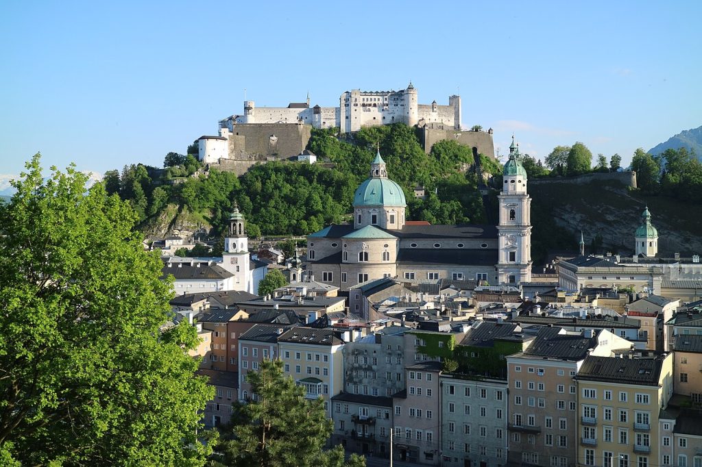 Hohensalzburg fortress on its wooded hill above the old town, seen from the Kapuzinerberg in early-evening sun