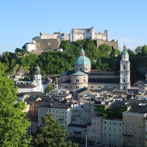 Hohensalzburg fortress on its wooded hill above the old town, seen from the Kapuzinerberg in early-evening sun