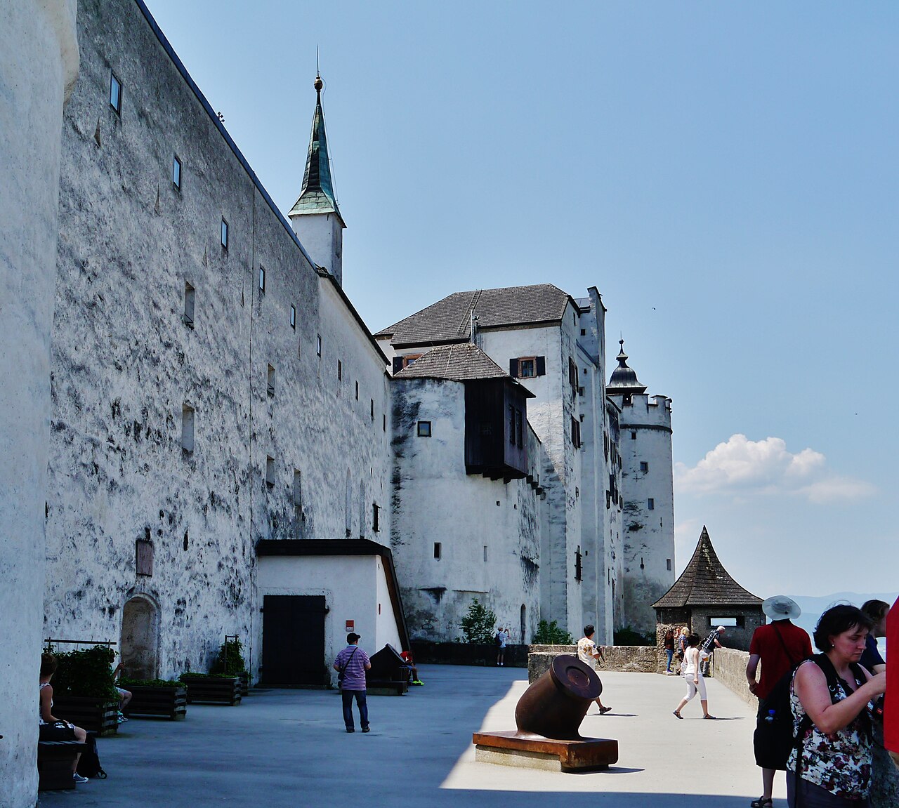A broad paved viewing terrace of the fortress below the high white walls of the inner castle, with a small mortar on a timber base and a sentry box wi