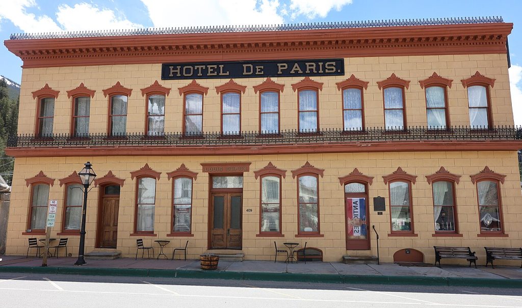 A long two-story building with a gray stucco front scored like stone blocks, an iron balcony and a sign reading Hotel de Paris.