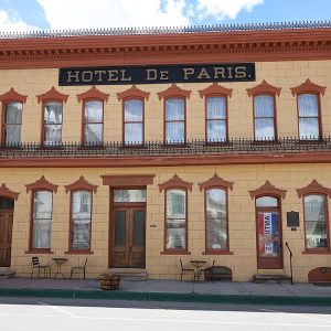 A long two-story building with a gray stucco front scored like stone blocks, an iron balcony and a sign reading Hotel de Paris.