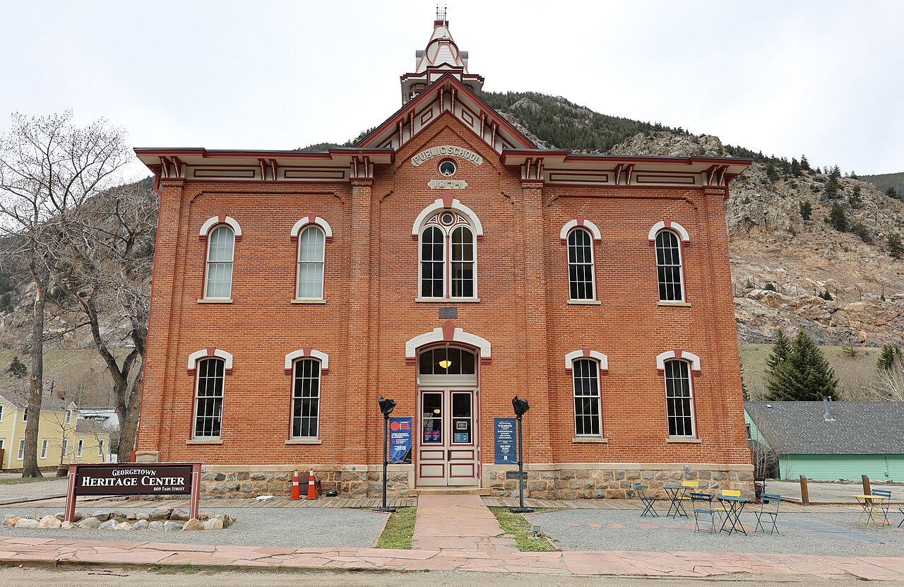 A two-story red-brick schoolhouse with Public School and 1874 on its central gable and a tiered bell tower on the roof.