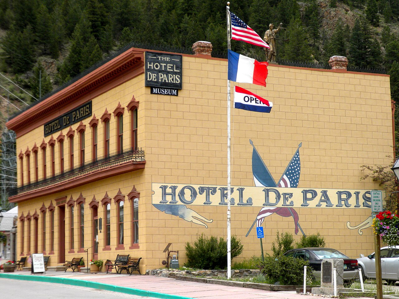 The corner of a stuccoed building with a painted mural of two crossed flags and a small gilded statue at the roofline.