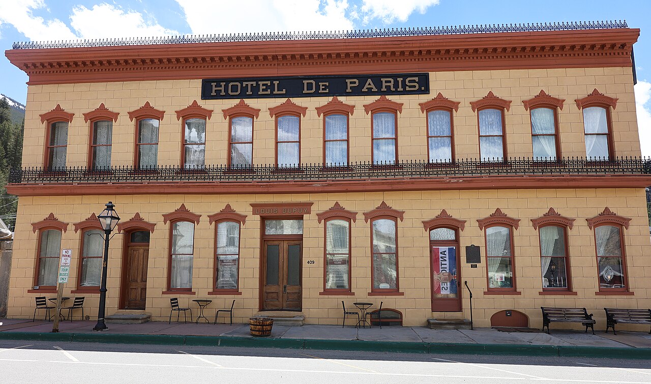 A long two-story building with a gray stucco front scored like stone blocks, an iron balcony and a sign reading Hotel de Paris.