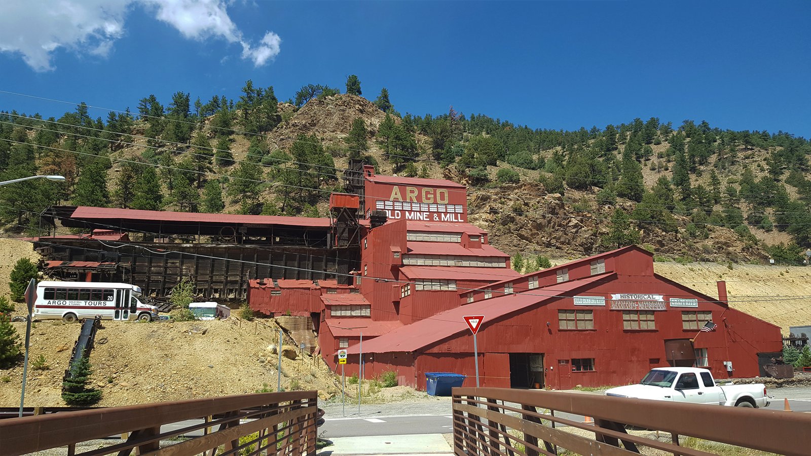 Red corrugated-iron mill buildings stepping up a hillside under a sign reading Argo Gold Mine and Mill.