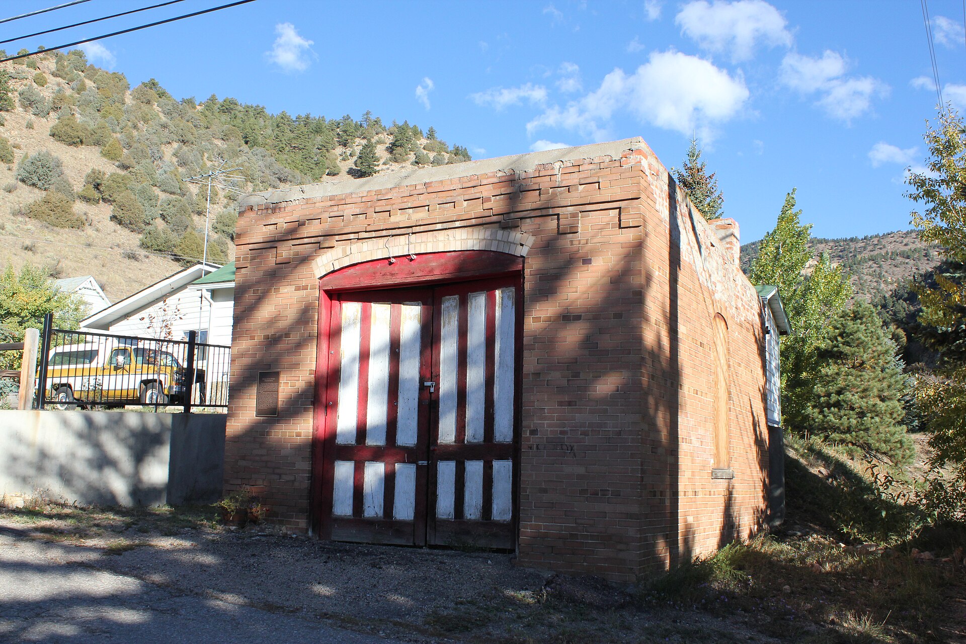 A small square red brick building with tall arched double doors painted in red and white stripes.