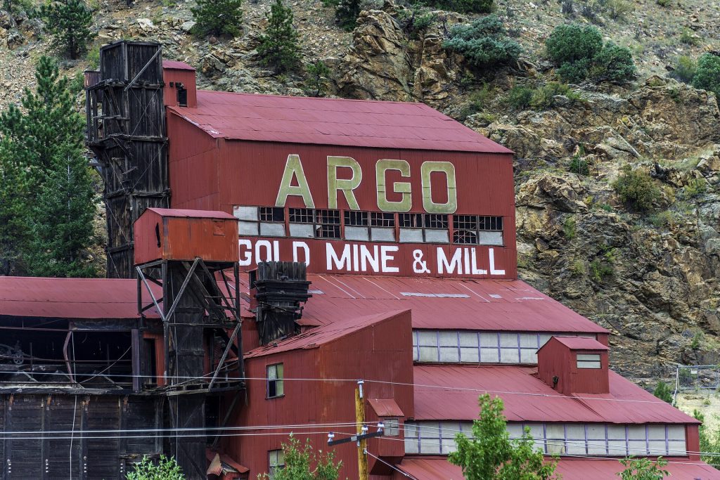 A tall red mill building painted Argo Gold Mine and Mill on a rocky hillside.