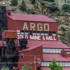 A tall red mill building painted Argo Gold Mine and Mill on a rocky hillside.