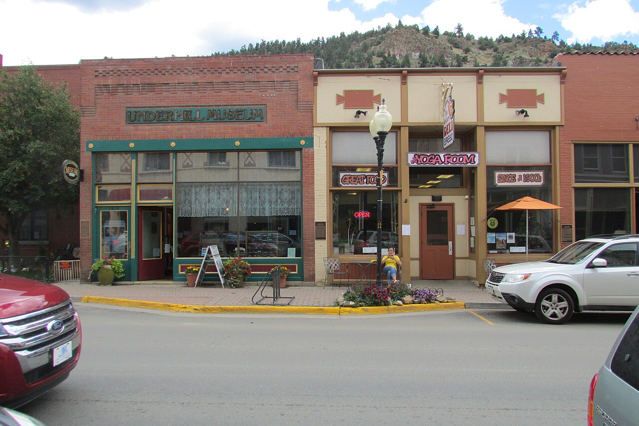 A low red brick storefront with a green sign, two doors side by side at the left and a large curtained window at the right.