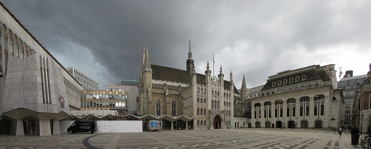 A wide paved yard under a dark sky, a curved dark band set into the paving in the foreground, Guildhall behind.