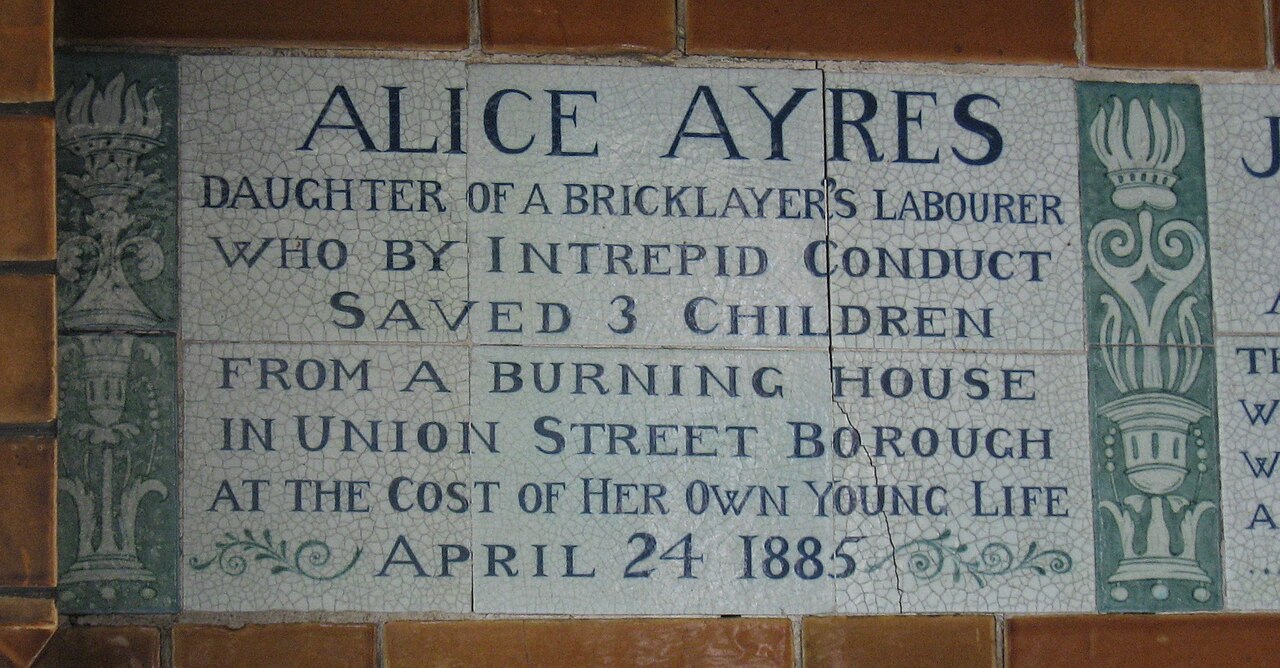 A white ceramic tablet with blue-green lettering naming Alice Ayres and a burning house in Union Street, 1885.