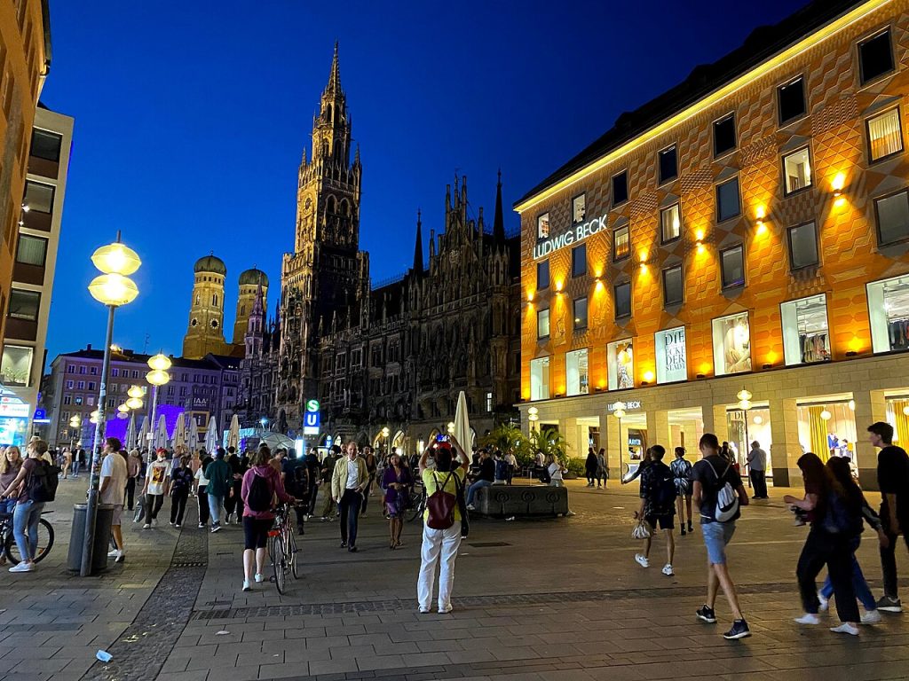 The Marienplatz at the blue hour under a deep blue sky: the floodlit Neues Rathaus with its tall tower at center, the two...