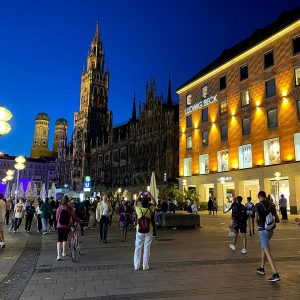 The Marienplatz at the blue hour under a deep blue sky: the floodlit Neues Rathaus with its tall tower at center, the two...