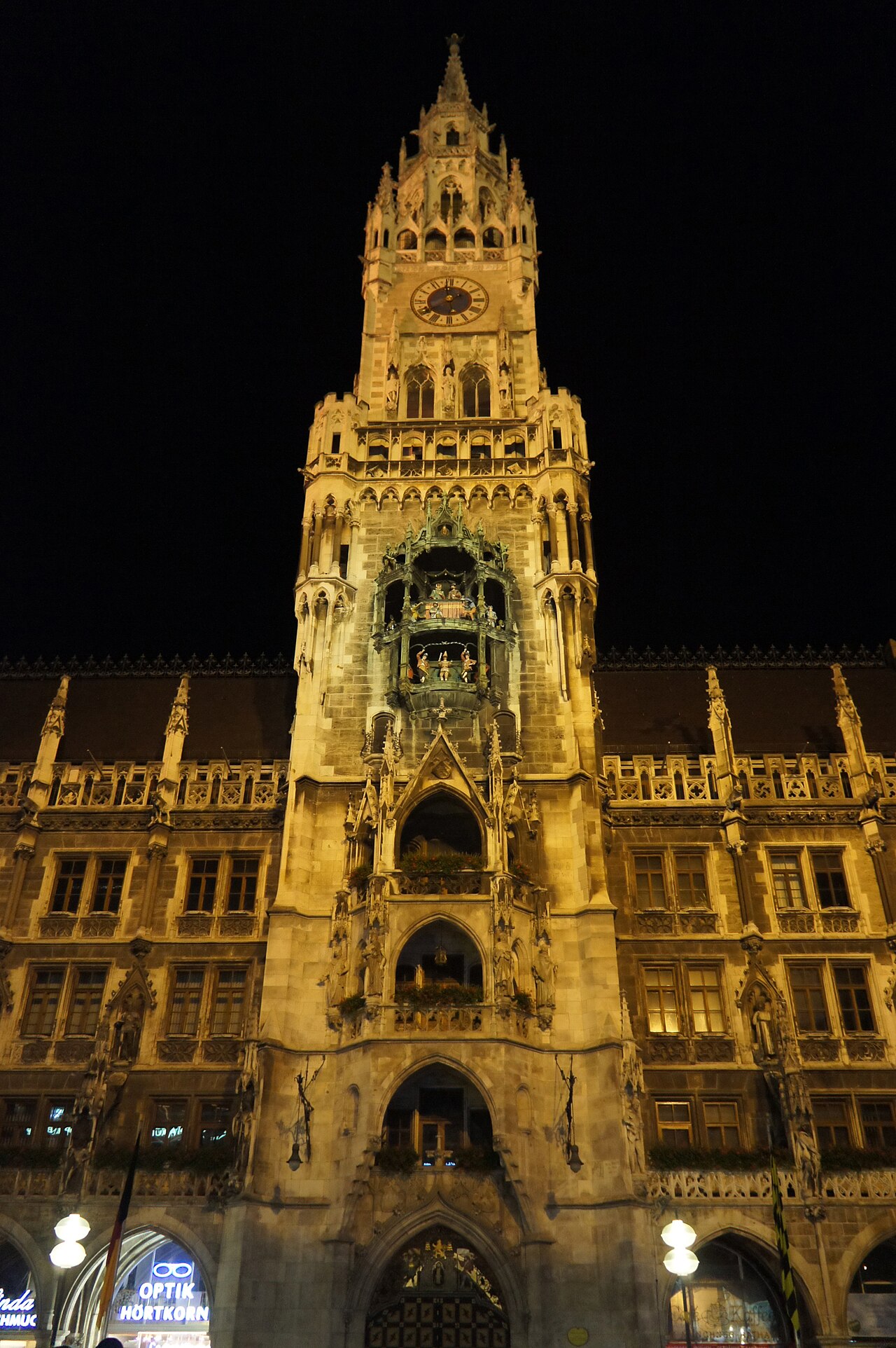 A floodlit neo-Gothic town hall tower against a black sky, with a bay of figures partway up.