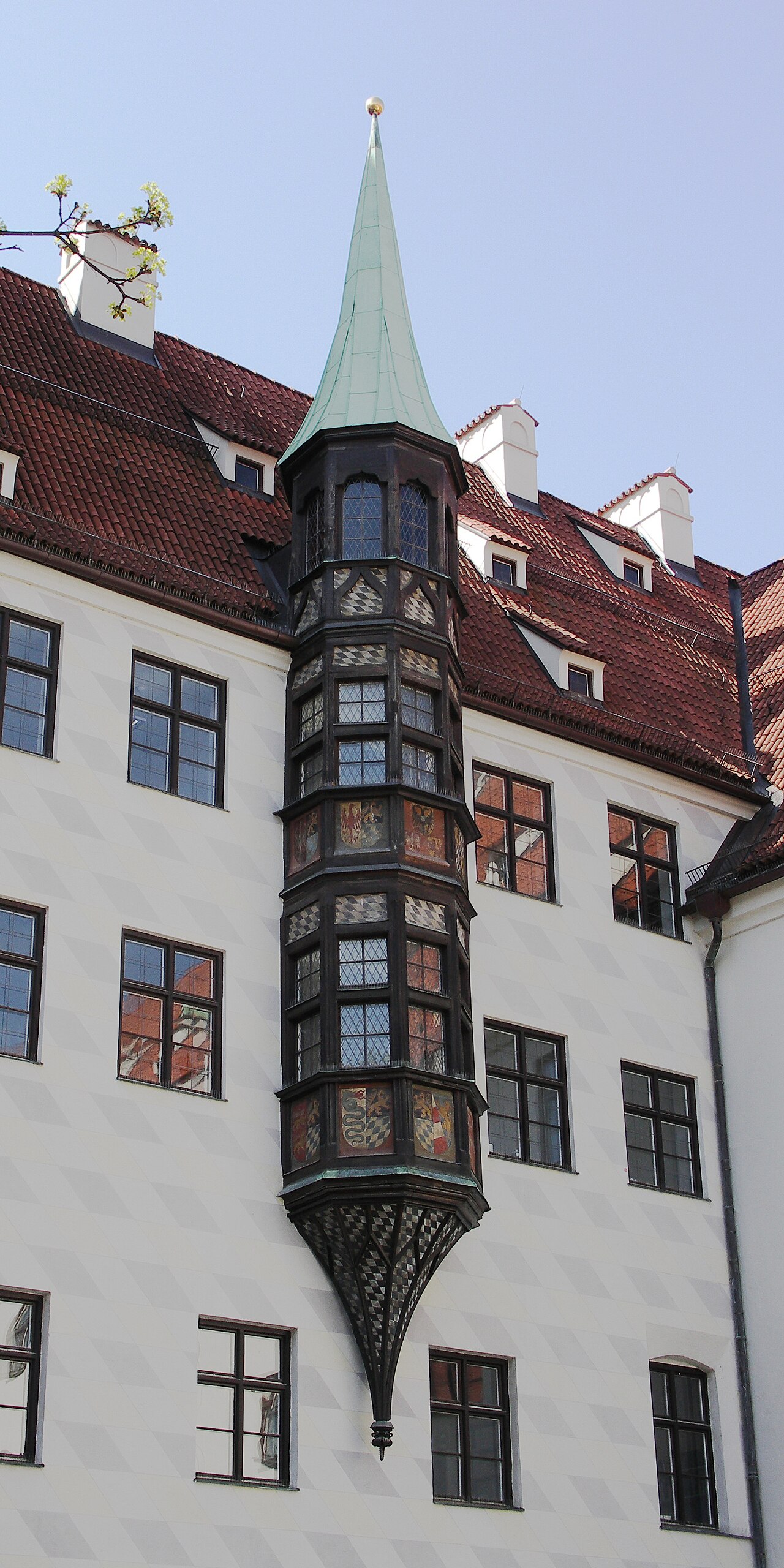 A slim dark timber-and-glass bay window climbing a white wall to a green spire.