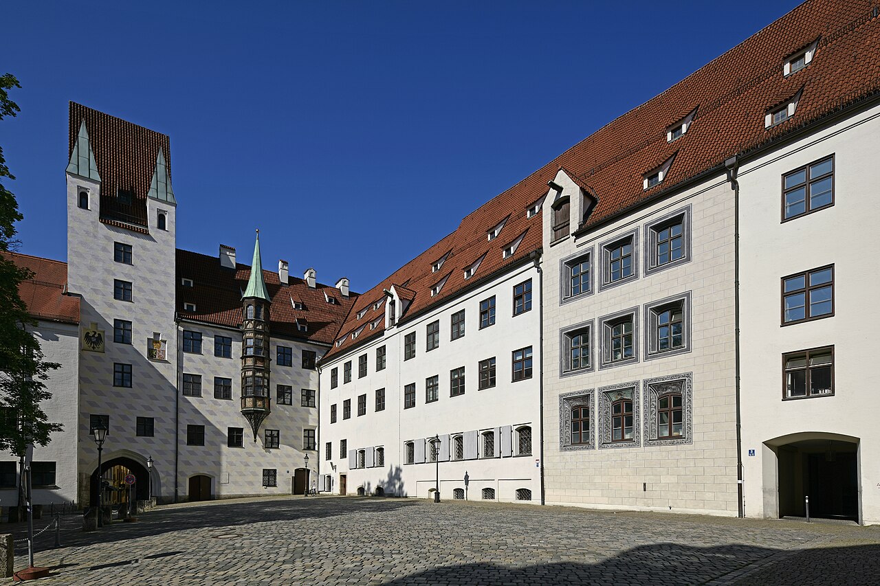 A cobbled courtyard with white wings, red roofs and a tower with a stepped gable.