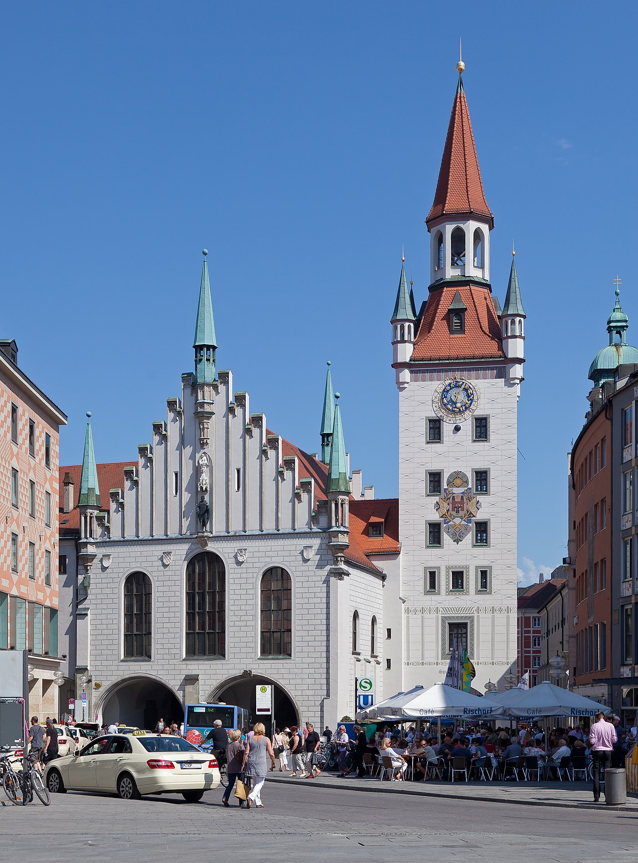 A white Gothic hall with a stepped gable and spires beside a tower with a clock and a red pointed roof.