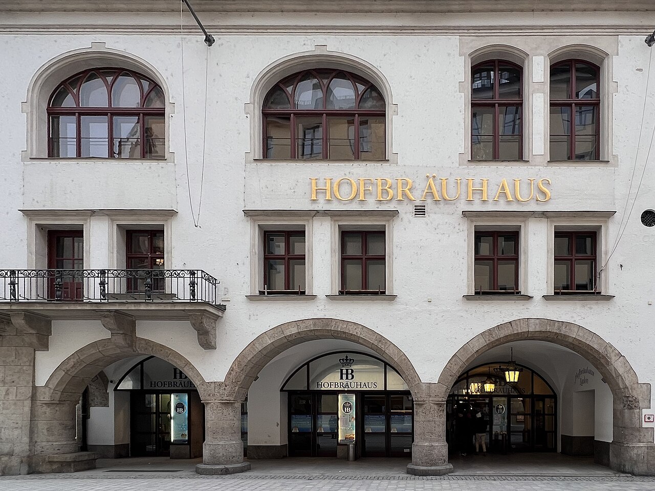 A white building front with three round arches at street level, a balcony and the name in gilt letters.