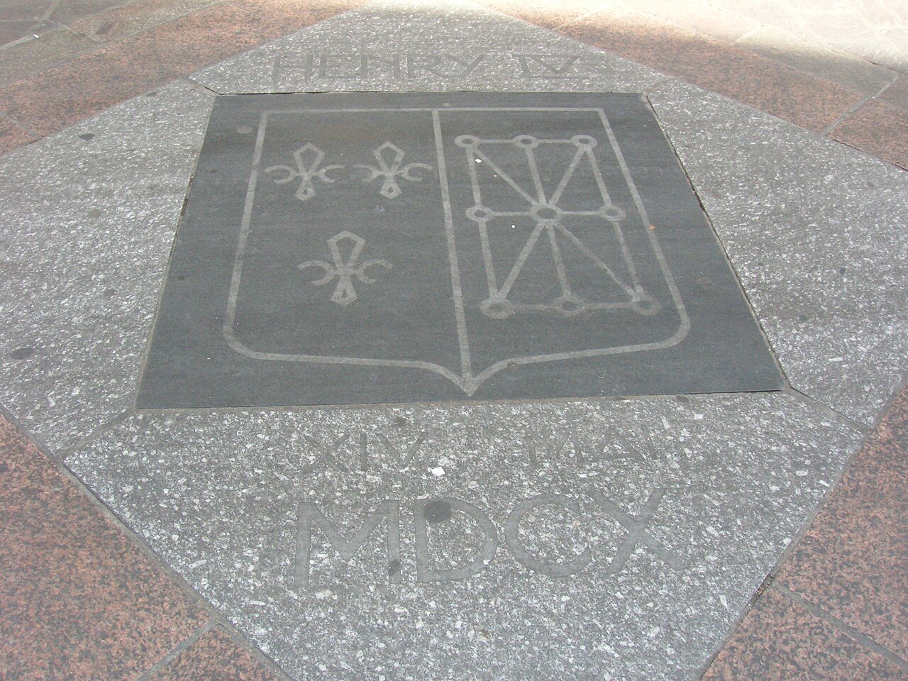 A stone shield with fleurs-de-lis and chains set into the surface of a street.