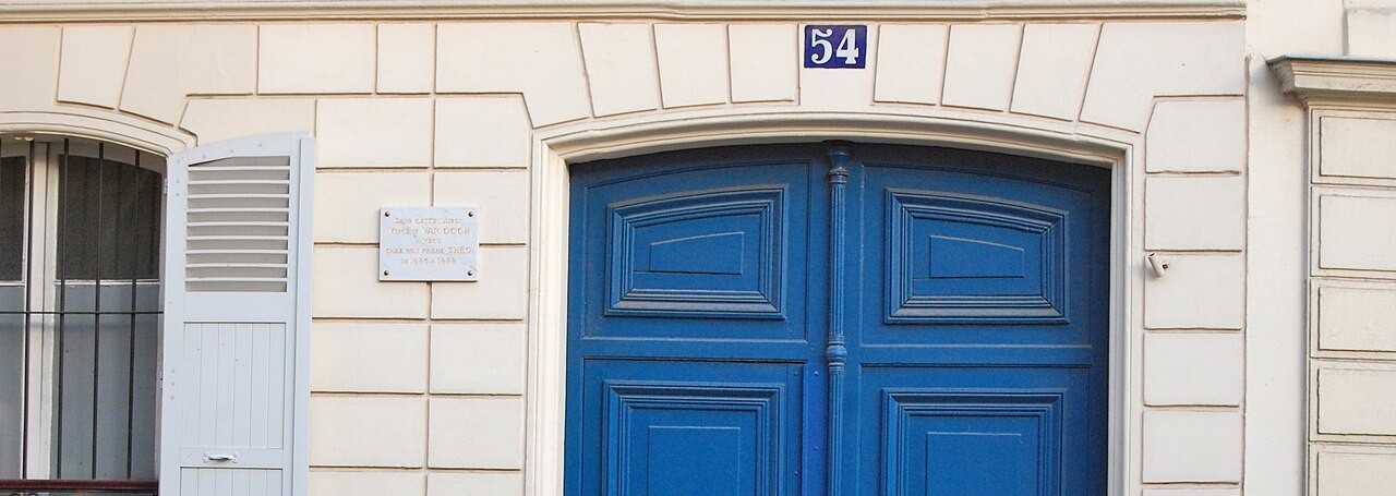 A tall blue carriage door below the house number 54, with a small marble plaque to its left.