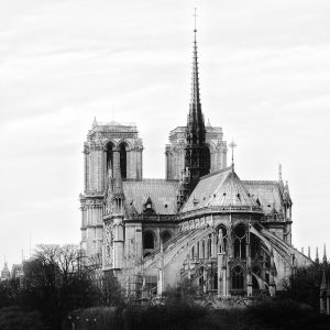 A black-and-white photograph of a cathedral's rounded east end ringed by flying buttresses, with a tall spire.