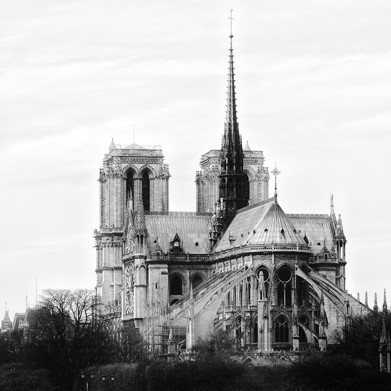 A black-and-white photograph of a cathedral's rounded east end ringed by flying buttresses, with a tall spire.