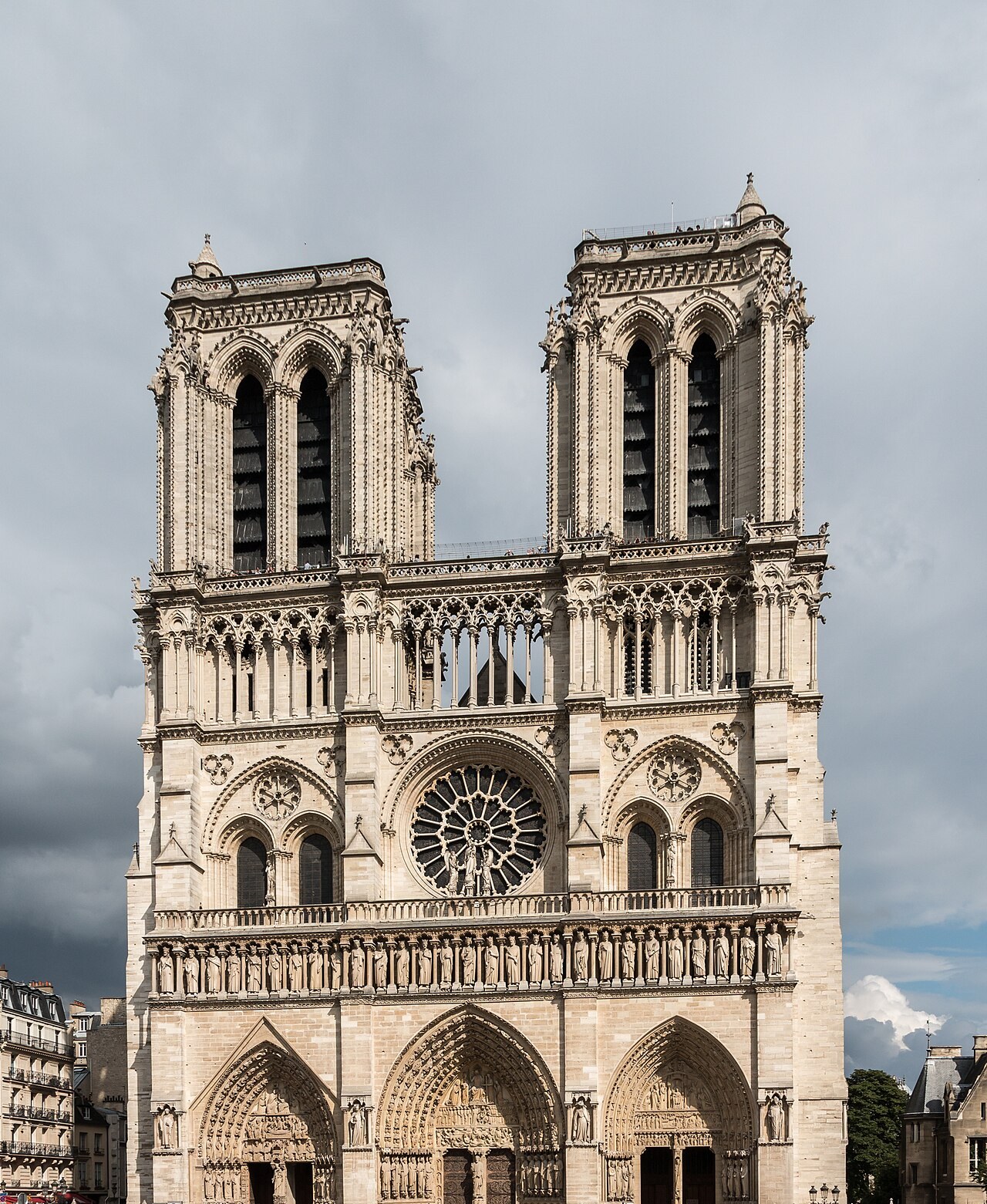 A pale Gothic facade with three deep doorways, a row of statues, a round rose window and two square towers.