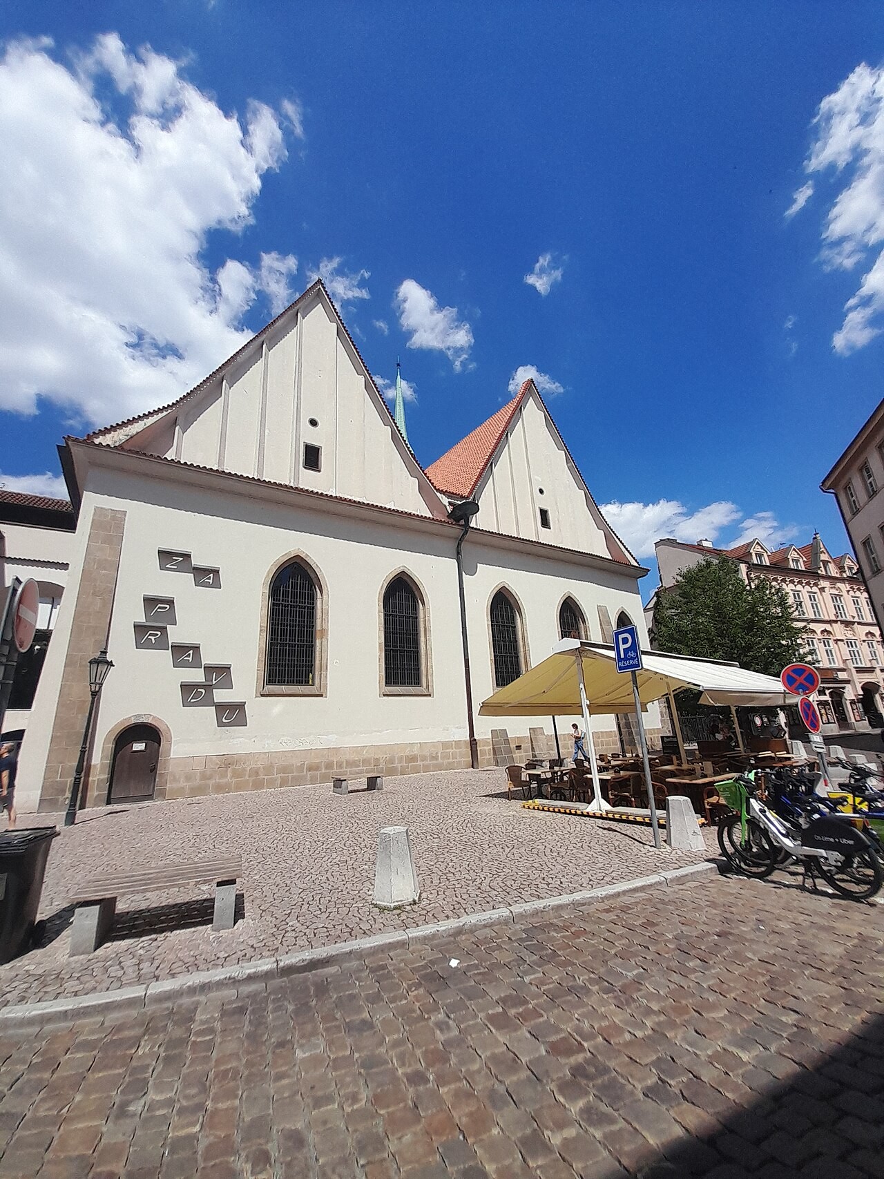A long white building with two steep gables over a paved square.