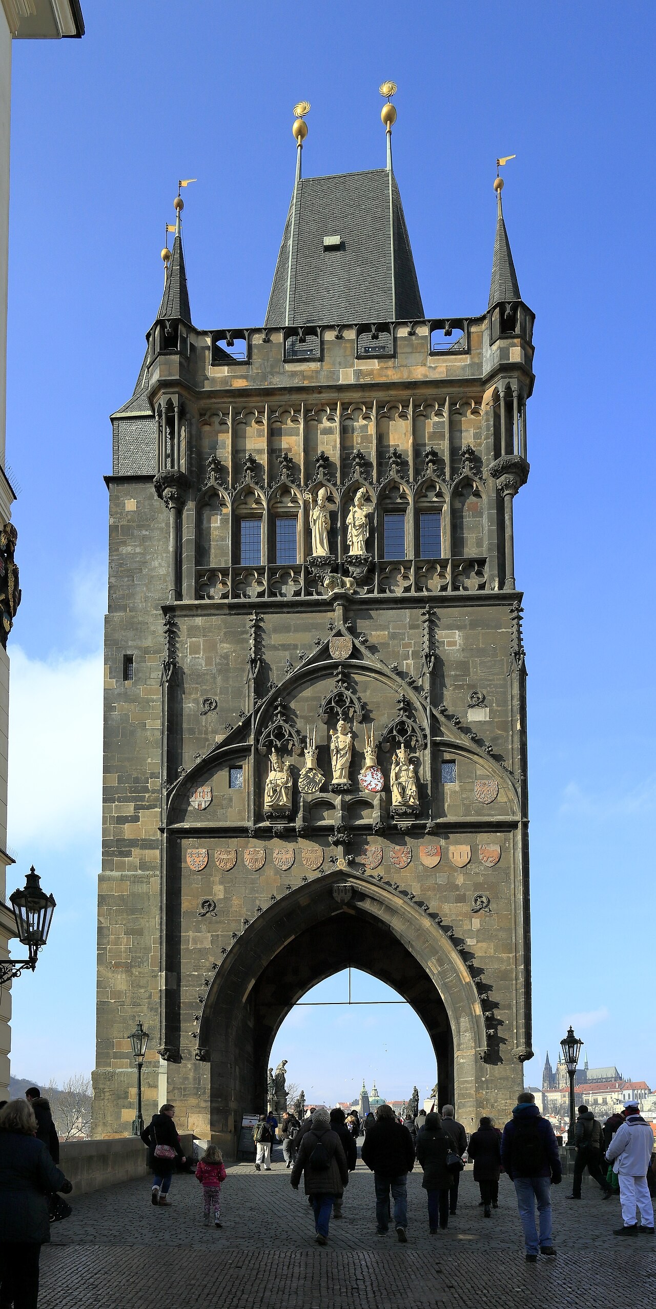 A tall Gothic gate tower with statues over a pointed archway and a narrow gallery under a steep slate roof.