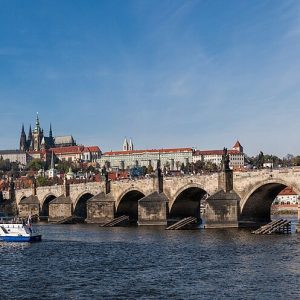 A long castle on a hill with a Gothic cathedral, above red roofs and a stone bridge over a river.