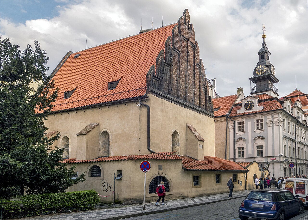 A steep stepped brick gable over a tall red-tiled roof, with a clock tower behind at right.