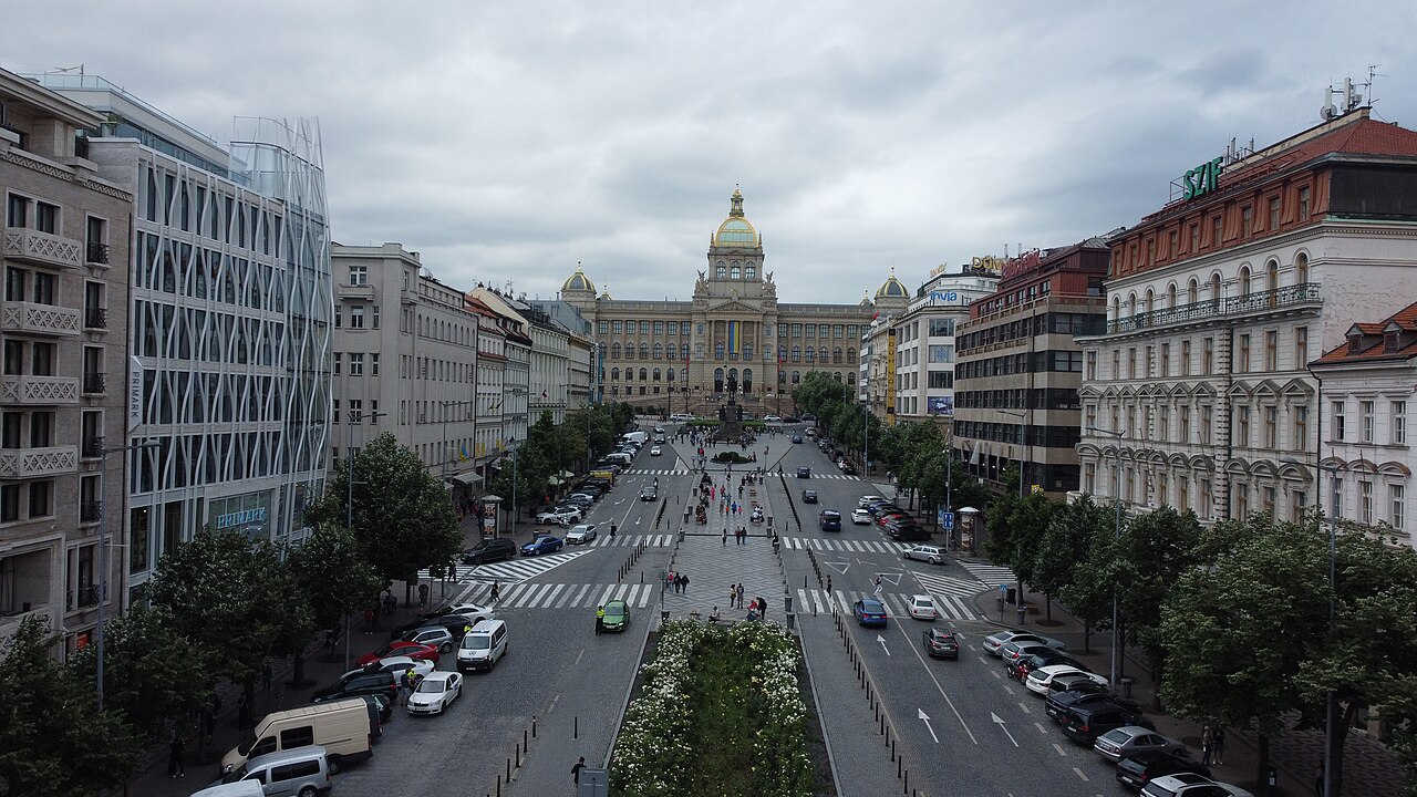 An elevated view up a long square with roads and a planted center strip to a domed museum.
