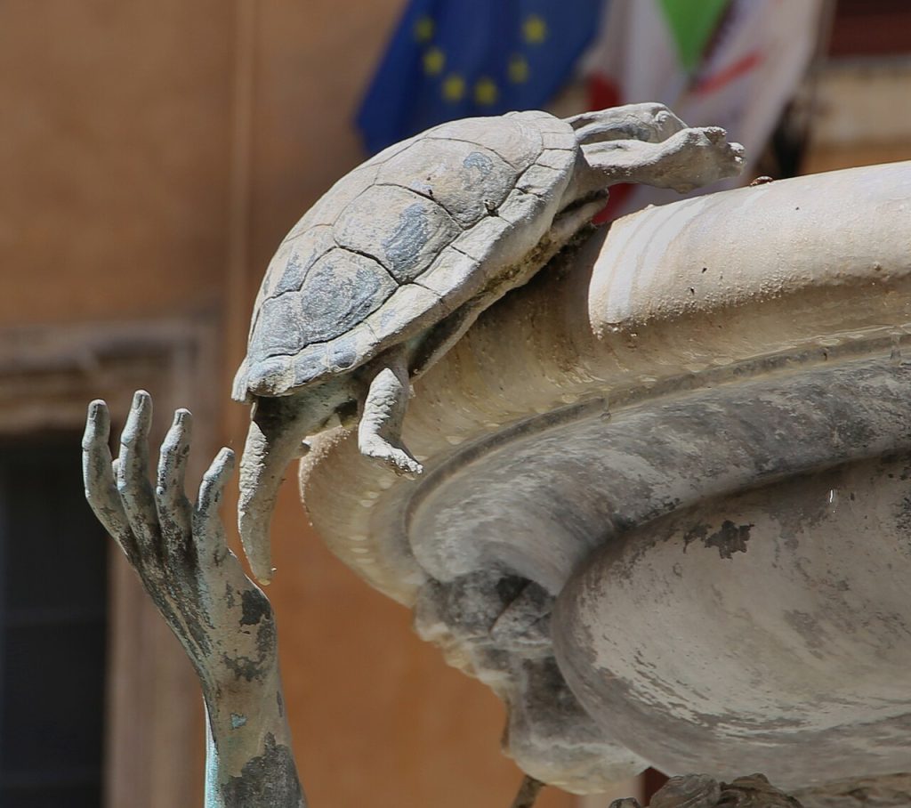 Close view of a bronze boy with one hand on a small bronze turtle at the edge of a marble basin.