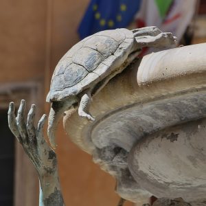 Close view of a bronze boy with one hand on a small bronze turtle at the edge of a marble basin.