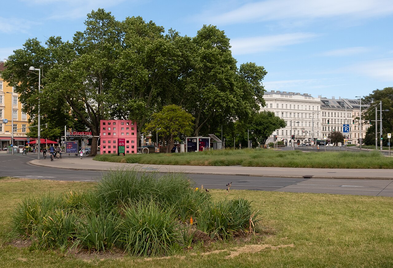 Lawns and trees in a small city park, with apartment buildings beyond.