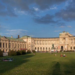 A long curved colonnaded palace front in low sun, with an equestrian statue on the square.
