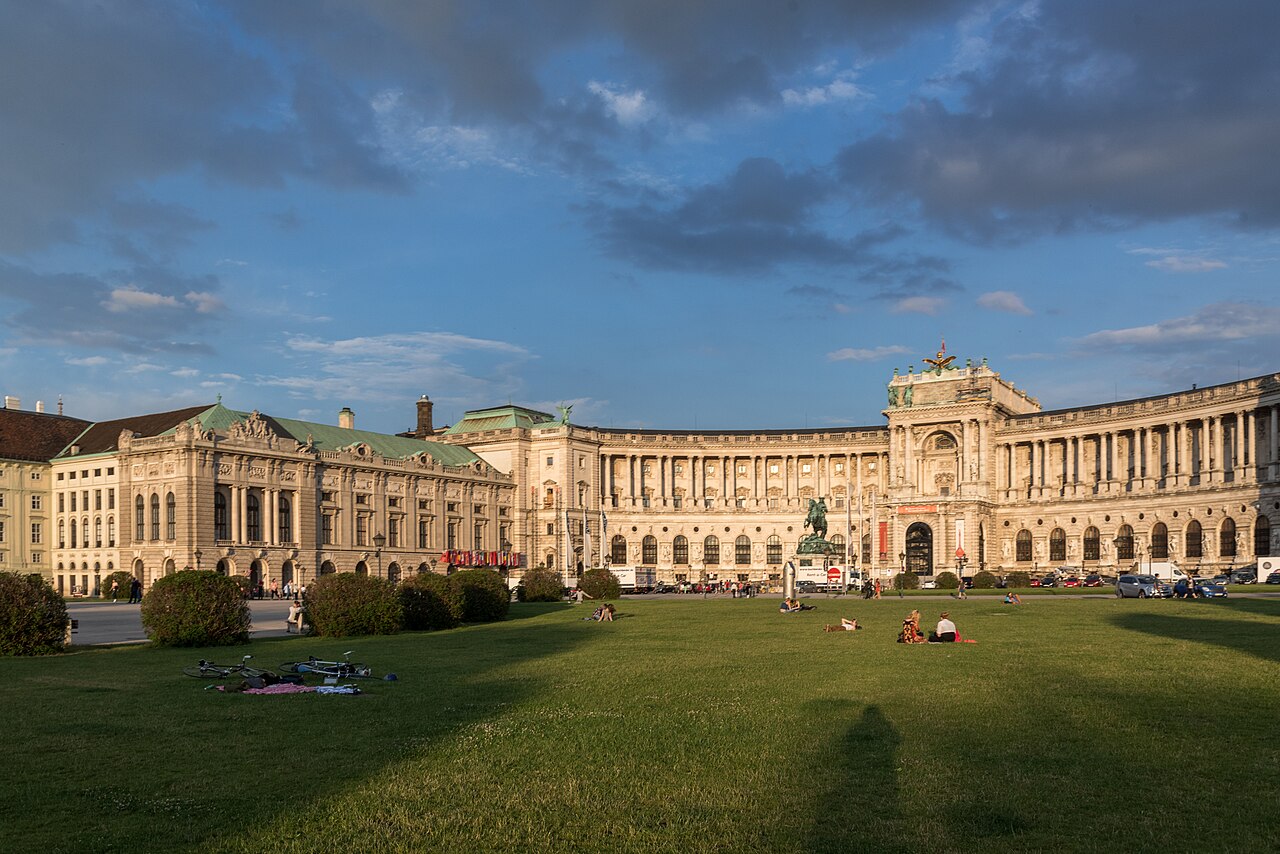 A long curved colonnaded palace front in low sun, with an equestrian statue on the square.