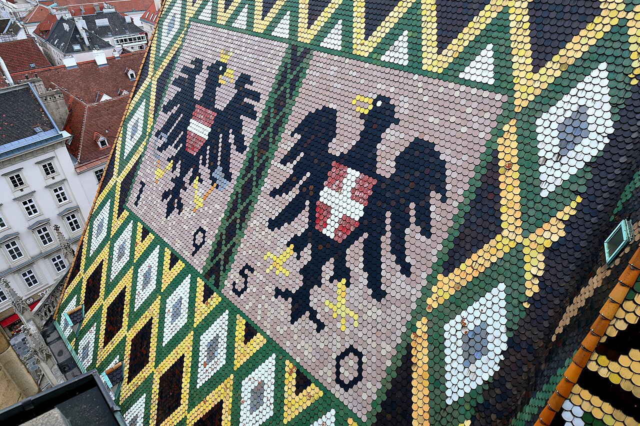Two black eagles with red and white shields laid out in colored roof tiles on a steep roof.